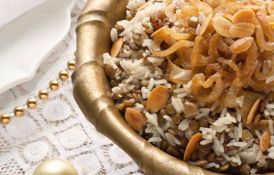 Fotografia em tons de marrom e dourado em uma mesa de madeira com uma toalha branca de renda com um recipiente redondo fundo e grande dourado com o arroz de festa com lentilhas. Fotografia em tons de marrom e dourado em uma mesa de madeira com uma toalha branca de renda com um recipiente redondo fundo e grande dourado com o arroz de festa com lentilhas.