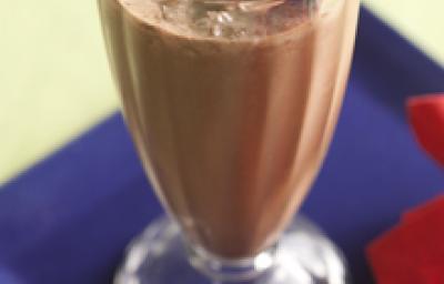 Fotografia em tons de azul e vermelho em uma mesa de madeira com um prato quadrado azul e um pano vermelho ao lado. Em cima do prato, uma taça de vidro com o milkshake Nescau crocante. Fotografia em tons de azul e vermelho em uma mesa de madeira com um prato quadrado azul e um pano vermelho ao lado. Em cima do prato, uma taça de vidro com o milkshake Nescau crocante.