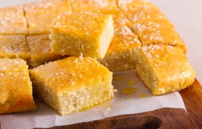 Fotografia em tons de amarelo com uma tábua ao centro. Em cima da tábua existe vários pedaços de bolo de cor amarela ao centro. Os pedaços de bolo estão cobertos com uma calda e coco ralado Fotografia em tons de amarelo com uma tábua ao centro. Em cima da tábua existe vários pedaços de bolo de cor amarela ao centro. Os pedaços de bolo estão cobertos com uma calda e coco ralado