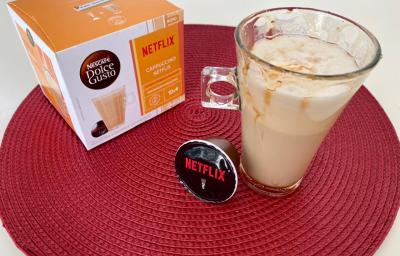 Fotografia em tons de laranja e vermelho com um copo de vidro ao centro. Dentro do copo existe uma receita de cappuccino com calda de caramelo e ao lado uma caixa de cápsulas Dolce Gusto Cappuccino NETFLIX Caramelo Salgado Fotografia em tons de laranja e vermelho com um copo de vidro ao centro. Dentro do copo existe uma receita de cappuccino com calda de caramelo e ao lado uma caixa de cápsulas Dolce Gusto Cappuccino NETFLIX Caramelo Salgado