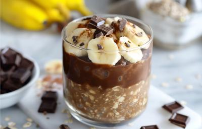 Fotografia em tons de amarelo com um copo de vidro ao centro. Dentro do copo existe uma receita de Overnight Oats com Banana e NINHO Adulto Fotografia em tons de amarelo com um copo de vidro ao centro. Dentro do copo existe uma receita de Overnight Oats com Banana e NINHO Adulto