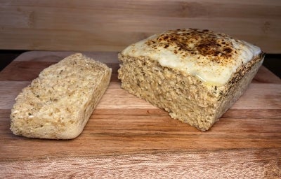 Fotografia de um pãozinho de aveia com queijo sobre uma tábua de madeira com uma fatia cortada. Fotografia de um pãozinho de aveia com queijo sobre uma tábua de madeira com uma fatia cortada.