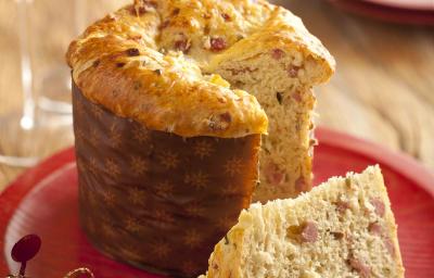 Fotografia em tons de vermelho e marrom, ao centro prato vermelho com um panetone fatiado, ao lado duas taças com bebida e uma decoração de natalina, ao fundo dois pratos empilhados, tudo sobre bancada de madeira rústica. Fotografia em tons de vermelho e marrom, ao centro prato vermelho com um panetone fatiado, ao lado duas taças com bebida e uma decoração de natalina, ao fundo dois pratos empilhados, tudo sobre bancada de madeira rústica.