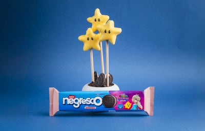 Cake pops em formato de estrela cobertos com chocolate amarelo, palitos e biscoitos Negresco ao fundo