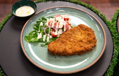 Milanesa uruguaia crocante no prato com salada de rúcula, tomate, cebola e aioli