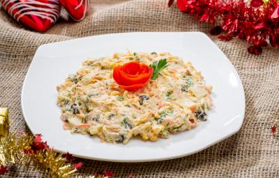 Fotografia de um salpicão tradicional cremoso com frango, cenoura, salsinha e uva passa em um prato branco quadrado. Por cima da salada, um tomate em formato de rosa e ao lado, uma folha de salsinha. Ao redor, decorações de Natal. Fotografia de um salpicão tradicional cremoso com frango, cenoura, salsinha e uva passa em um prato branco quadrado. Por cima da salada, um tomate em formato de rosa e ao lado, uma folha de salsinha. Ao redor, decorações de Natal.