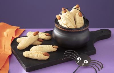 Foto em tons de roxo da receita de biscoito amanteigado de dedo de zumbi servida em diversas porções dentro de um caldeirão preto sobre uma tábua preta com mais algumas porções ao lado Foto em tons de roxo da receita de biscoito amanteigado de dedo de zumbi servida em diversas porções dentro de um caldeirão preto sobre uma tábua preta com mais algumas porções ao lado