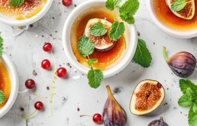 Fotografia vista de cima em tons claros de quatro recipientes brancos fundos com uma sobremesa de figos frescos flambados, com NESTLÉ Creme de Leite. Por cima das sobremesas tem metade de um figo e hortelã, ao redor tem figos, hortelã e cerejas. Fotografia vista de cima em tons claros de quatro recipientes brancos fundos com uma sobremesa de figos frescos flambados, com NESTLÉ Creme de Leite. Por cima das sobremesas tem metade de um figo e hortelã, ao redor tem figos, hortelã e cerejas.