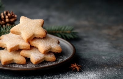 Em cima de uma mesa, prato redondo com biscoitos em formato de estrelas, decorados com açúcar de confeiteiro. Em cima de uma mesa, prato redondo com biscoitos em formato de estrelas, decorados com açúcar de confeiteiro.