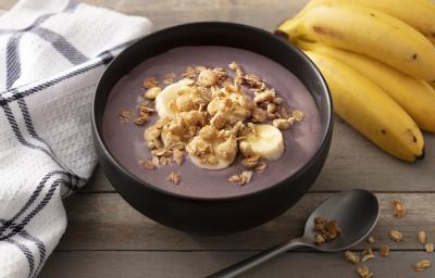 Fotografia em tons de branco e preto de uma bancada branca, sobre ela um recipiente redondo preto com açaí, um cacho de banana, uma colher e um paninho branco com listras pretas. Fotografia em tons de branco e preto de uma bancada branca, sobre ela um recipiente redondo preto com açaí, um cacho de banana, uma colher e um paninho branco com listras pretas.