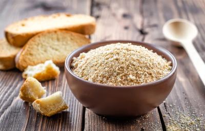 Fotografia em tons claros de um recipiente pequeno e fundo marrom sobre uma mesa de madeira escura. Ao lado do recipiente tem alguns pedaços de pão, e no fundo tem três fatias de pão.