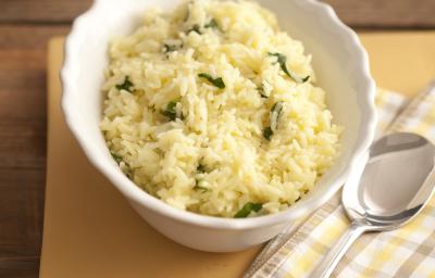 Fotografia em tons de amarelo em uma bancada de madeira com um pano listrado em em bege e amarelo e um prato fundo branco com o arroz com rúcula. Fotografia em tons de amarelo em uma bancada de madeira com um pano listrado em em bege e amarelo e um prato fundo branco com o arroz com rúcula.