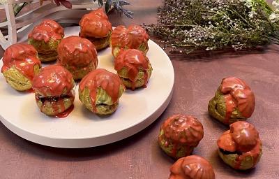 Foto em tons de vermelho da receitas de carolinas de frutas vermelhas servidas em diversas porções, algumas sobre uma base redonda branca e outras sobre a mesa vermelha. Ao fundo há flores para decoração Foto em tons de vermelho da receitas de carolinas de frutas vermelhas servidas em diversas porções, algumas sobre uma base redonda branca e outras sobre a mesa vermelha. Ao fundo há flores para decoração