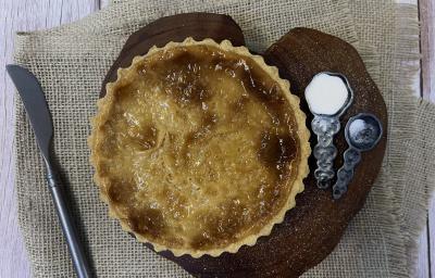 Foto vista de cima da receita de Torta de Leite Moça, sobre uma tábua de madeira, com duas colheres de ferro ao lado, uma delas com açúcar. Abaixo da tábua há um tecido e sobre ele uma faca do lado esquerdo. Foto vista de cima da receita de Torta de Leite Moça, sobre uma tábua de madeira, com duas colheres de ferro ao lado, uma delas com açúcar. Abaixo da tábua há um tecido e sobre ele uma faca do lado esquerdo.