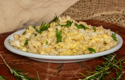 Fotografia em tons de amarelo com um prato branco ao centro. Em cima do prato existe uma receita de farofa de ovos feita com farinha de mandioca e finalizada com cheiro-verde.
