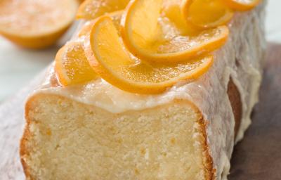 Fotografia de um bolo de laranja feito em forma retangular, com cobertura e rodelas finas de laranja. O bolo está sobre uma tábua de madeira. Fotografia de um bolo de laranja feito em forma retangular, com cobertura e rodelas finas de laranja. O bolo está sobre uma tábua de madeira.