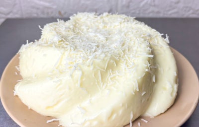 fotografia em tons claros de um manjar de coco ao centro. Por cima do manjar, existe alguns pedaços de flocos de coco