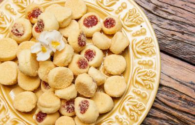 Fotografia de um prato amarelo de vidro sobre uma mesa de madeira. Dentro do prato tem várias unidades de biscoitos amanteigados com goiabada. Fotografia de um prato amarelo de vidro sobre uma mesa de madeira. Dentro do prato tem várias unidades de biscoitos amanteigados com goiabada.