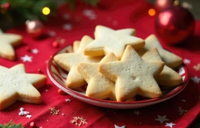 Em cima de uma mesa decorada com bolinhas de natal, prato vermelho redondo com biscoitos em formato de estrelas.