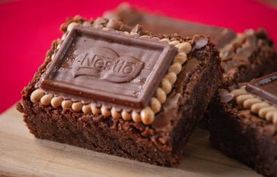 Fotografia três unidades de brownies com biscoito choco biscuit, eles estão apoiados um no outro e sobre uma tábua de madeira. O fundo da foto é vermelho. Fotografia três unidades de brownies com biscoito choco biscuit, eles estão apoiados um no outro e sobre uma tábua de madeira. O fundo da foto é vermelho.