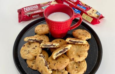 Fotografia de um prato preto servido de cookies e uma xícara vermelha com leite dentro.