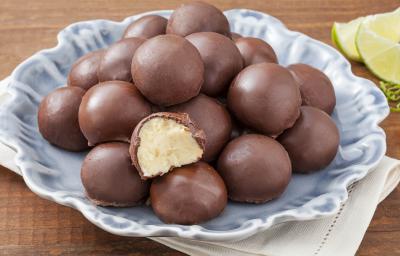 Fotografia em tons de marrom e azul de uma bancada de marrom com um paninho branco, sobre ele um prato azul com trufas. Ao fundo fatias de limão.