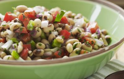 Fotografia de uma salada de feijão branco com vinagrete em um refratário de vidro na cor verde, tom claro sobre uma mesa de madeira. Ao lado, uma colher pequena de madeira em tom escuro sobre uma toalha de mesa dobrada na cor verde e branco. Fotografia de uma salada de feijão branco com vinagrete em um refratário de vidro na cor verde, tom claro sobre uma mesa de madeira. Ao lado, uma colher pequena de madeira em tom escuro sobre uma toalha de mesa dobrada na cor verde e branco.