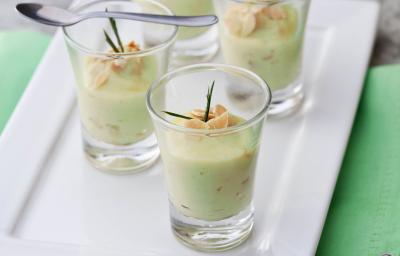 Fotografia em tons de verde em uma bancada de madeira com guardanapo verde, um prato retangular branco raso ao centro com quatro copinhos de vidro com o brigadeiro de capim-santo e lascas de amêndoas dentro deles. Fotografia em tons de verde em uma bancada de madeira com guardanapo verde, um prato retangular branco raso ao centro com quatro copinhos de vidro com o brigadeiro de capim-santo e lascas de amêndoas dentro deles.