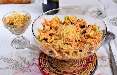 Em cima de uma mesa, tigela com frango desfiado cremoso, cenouras raladas, uvas-passas e batata-palha.