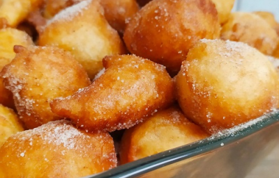 Foto da receita de Bolinho de chuva sem ovo. Observa-se um refratário quadrado de vidro transparente com os bolinhos fritos e polvilhados de açúcar dentro. Foto da receita de Bolinho de chuva sem ovo. Observa-se um refratário quadrado de vidro transparente com os bolinhos fritos e polvilhados de açúcar dentro.