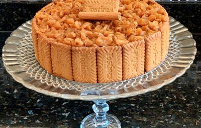 Fotografia de uma torta de biscoitos tostines, creme belga e abacaxi caramelizado. Por volta da torta tem vários tostines inteiros, e por cima, tem abacaxi em pedaços pequenos, canela em pau e mais tostines. A torta está sobre um apoio de vidro.