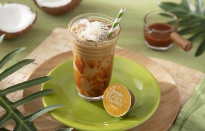 Foto da receita de iced coffee coco com caramelo servida em um copo de vidro alto com um canudo listrado verde em cima de um prato verde sobre uma tábua de madeira Foto da receita de iced coffee coco com caramelo servida em um copo de vidro alto com um canudo listrado verde em cima de um prato verde sobre uma tábua de madeira