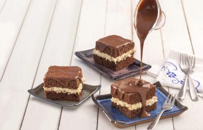 Fotografia em tons de azul em uma bancada de madeira branca, um paninho branco com detalhes azul, três pratinhos com pedaços do bolo de prestígio com calda de chocolate.
