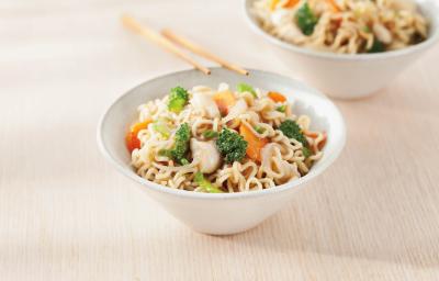 Foto de uma tigela branca com yakissoba de frango dentro e encostada nela há dois hashis. No fundo há outra tigela também com Yakissoba