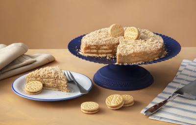 Foto de uma mesa marrom clara, com uma boleira azul escura. Sobre ela está a receita da Torta de Palha Italiana decorada com Biscoitos Bono Doce de Leite. Na mesa há um prato com uma fatia, mais alguns biscoitos Bono e guardanapos de tecido.