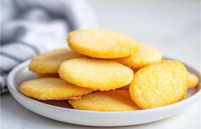 Fotografia em tons claros de um prato médio branco e raso com alguns biscoitos de maizena em formato de círculo. O prato está sobre uma mesa branca.