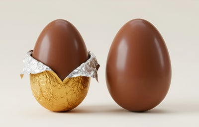 Fotografia em tons claros com dois ovos de páscoa veganos feitos com cacau em pó ao centro embrulhados em papel dourado