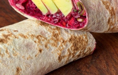 Fotografia em tons de marrom e vermelho de um wrap recheado de beterraba e cenoura.