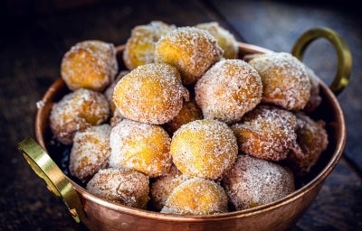 Em cima de uma mesa, balde de metal com bolinhos de chuva, polvilhado com açúcar de confeiteiro.