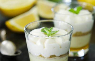 Fotografia de dois copinhos de vidro com farofa de biscoito e creme de limão sobre uma mesa de mármore preta. Ao fundo, duas metades de um limão siciliano, muitas folhas de hortelã e uma colher de sobremesa. Fotografia de dois copinhos de vidro com farofa de biscoito e creme de limão sobre uma mesa de mármore preta. Ao fundo, duas metades de um limão siciliano, muitas folhas de hortelã e uma colher de sobremesa.