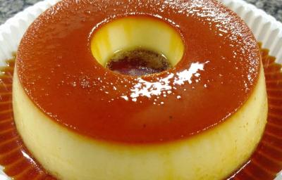 Fotografia em tons de bege em uma mesa de mármore, um prato branco redondo com o pudim de leite gourmet com calda de caramelo em cima dele. Fotografia em tons de bege em uma mesa de mármore, um prato branco redondo com o pudim de leite gourmet com calda de caramelo em cima dele.