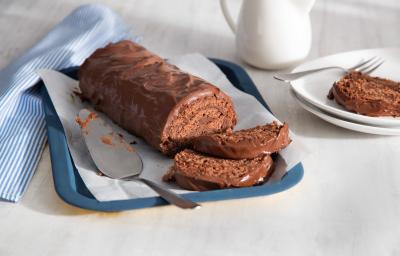 Fotografia em tons de azul, branco e marrom, ao centro da foto o rocambole todo de chocolate com 2 fatias na bandeja azul, ao lado está um prato branco com uma fatia do rocambole e do outro um guardanapo listrado de azul e branco. Fotografia em tons de azul, branco e marrom, ao centro da foto o rocambole todo de chocolate com 2 fatias na bandeja azul, ao lado está um prato branco com uma fatia do rocambole e do outro um guardanapo listrado de azul e branco.