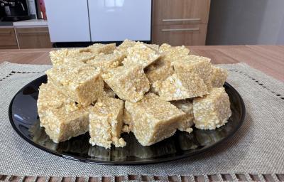 Fotografia em tons claros com vários quadradinhos feitos com amendoim, leite moça e tostines maisena ao centro. Os quadradinhos possuem cores caramelizadas e crocantes de amendoim e tostines