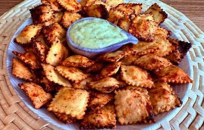 Fotografia mostra raviolis dourados sobre um prato branco. Ao centro, um molho verde.