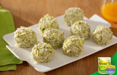 Snacks de brócolis em formato de bolinhas com queijo ralado, dispostos em prato branco sobre mesa de madeira.