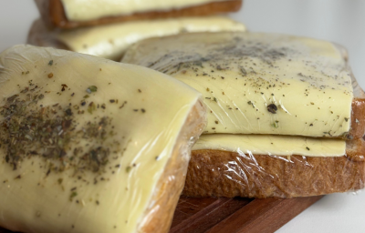 Fotografia mostra sanduíches embalados em plástico filme. As fatias de pão de forma aparecem cobertas por queijo com orégano polvilhado