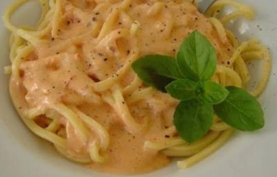 Fotografia em tons de vermelho, em uma bancada de madeira de cor marrom. Ao centro, um prato branco contendo o macarrão.