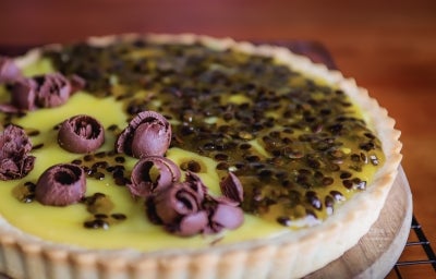 Fotografia da torta de maracujá com base crocante, recheio cremoso e cobertura de geleia natural da fruta. Decorada com raspas de chocolate, traz o contraste ideal entre acidez e dulçor. Uma sobremesa tropical e irresistível!