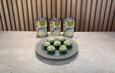 Prato cinza com docinhos verdes cobertos por granulado branco, acompanhado de latas de Leite Moça ao fundo.