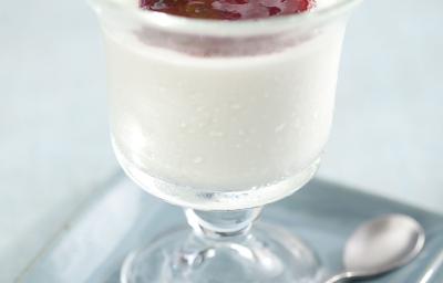 Fotografia em tons de cinza em uma mesa de madeira cinza com um prato quadrado azul claro e uma taça de vidro em cima com o mousse de iogurte com geleia de frutas vermelhas.